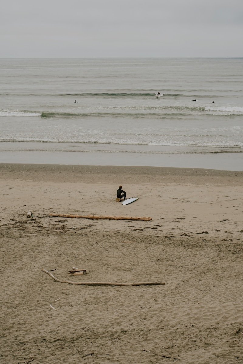 Surfer sits on beach with surfboard near ocean waves